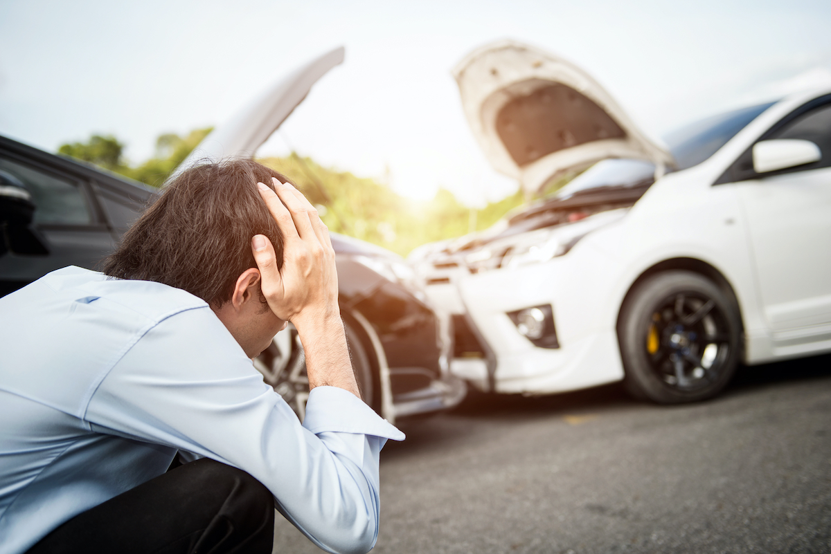 A man with his heads on his head looks at a car accident